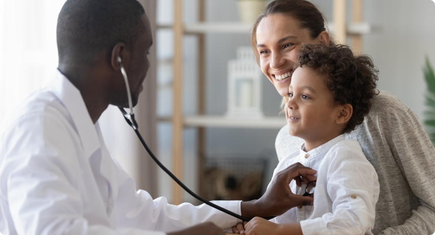 A mom holding her son while a doctor uses a stethoscope. 