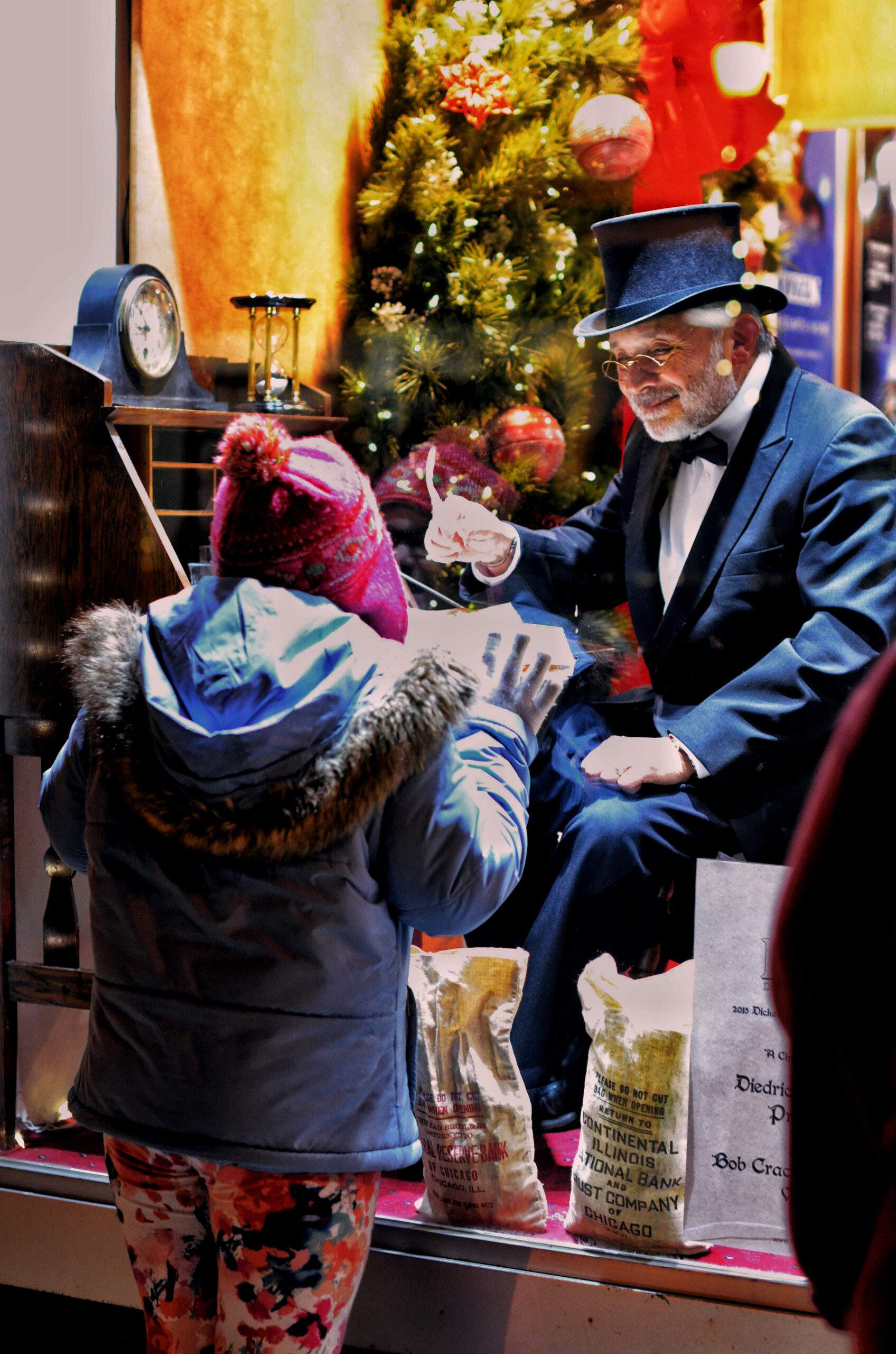 Man in tuxedo and top hat interacts with child in winter hat and jacket