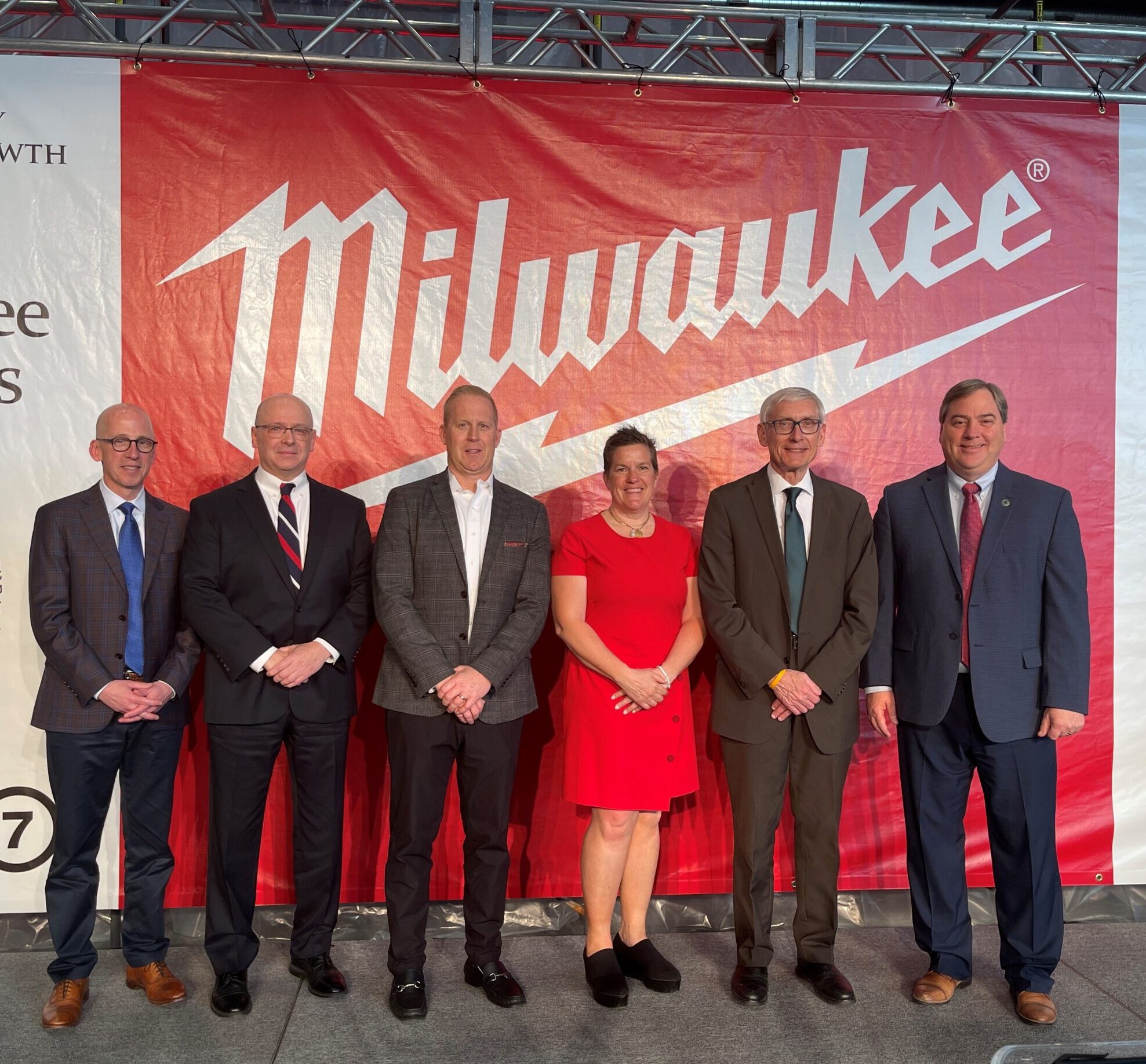 Five men and one woman stand in front of a banner.