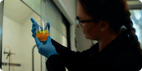 Female technician inspecting a chemical in a glass container.