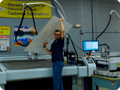 Inpro worker lifting a large sign off of a cutting machine.