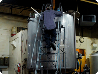 A worker climbing a ladder to access the top of a chemical tank.
