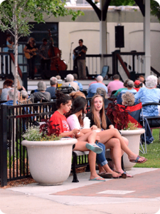 Three women sitting on a bench at an outdoor concert.