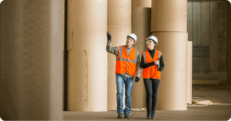 Two people reviewing giant roles of paper in a mill.