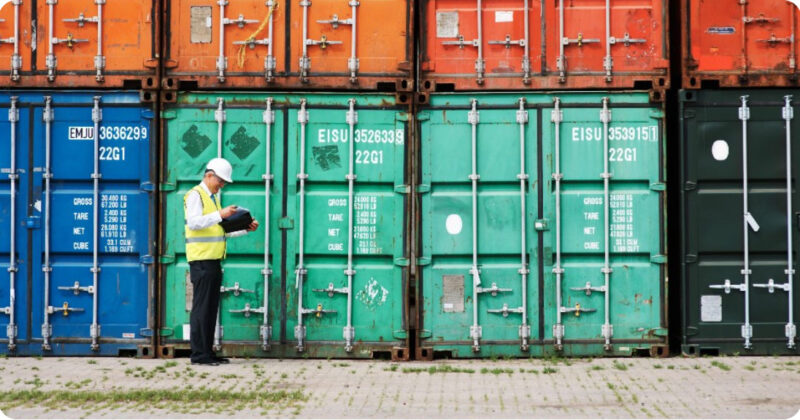 Man wearing a hard hat inspecting shipping containers.