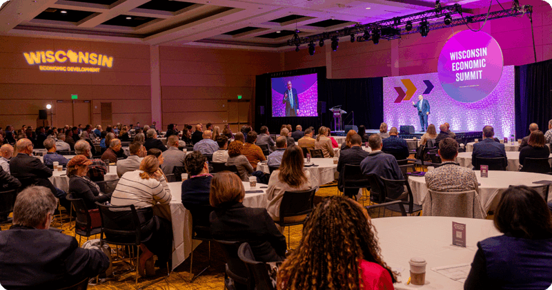 Participants at the 2025 Economic Summit sitting at round tables listening to speaker.