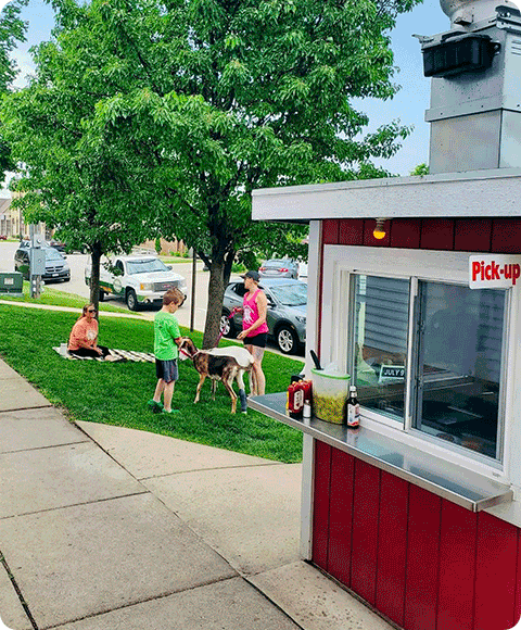 People with their dogs waiting for a meal outside of a food stand.