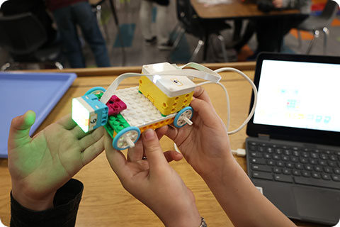 Student's hands holding a LEGO car they created in their Fab Lab class.