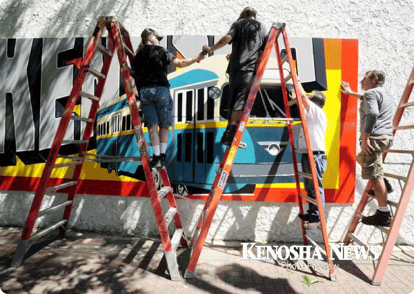 People on ladders painting a mural on a building in Kenosha.