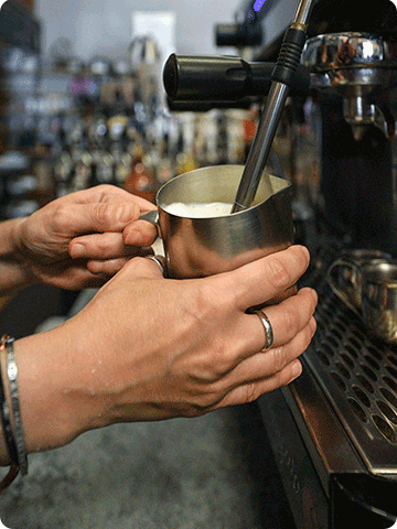 A closeup of a barista's hands steaming milk for a latte.