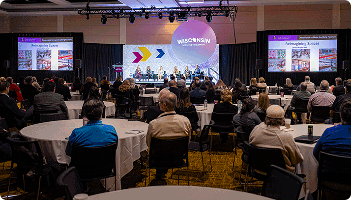 2025-Summit-panel-with-audience-714×407 Summit attendees listening to a panel discussion.