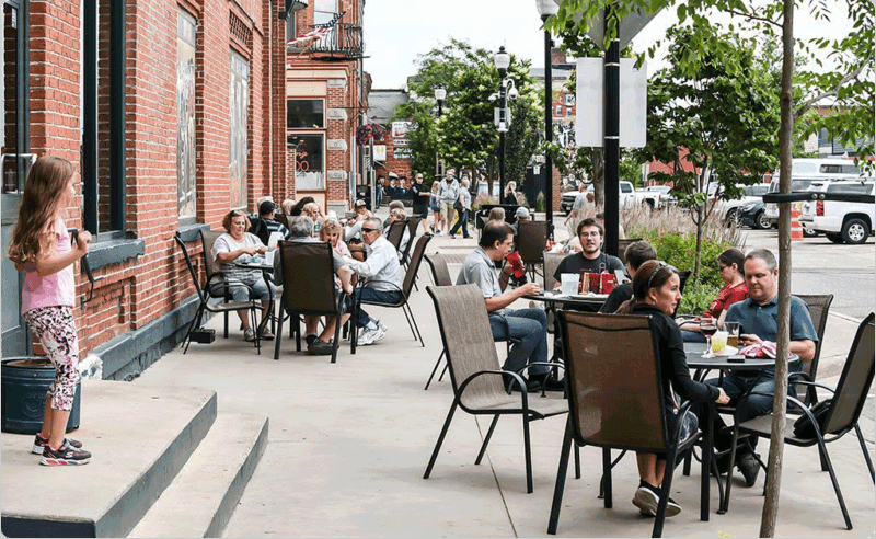People sitting at round tables on the sidewalk in Stevens Point.